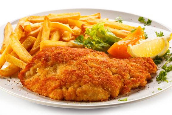 Pescado empanizado con papas fritas, ensalada y rodajas de limón.