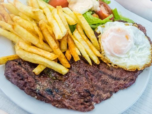Plato con carne asada, papas fritas, ensalada y un huevo frito.
